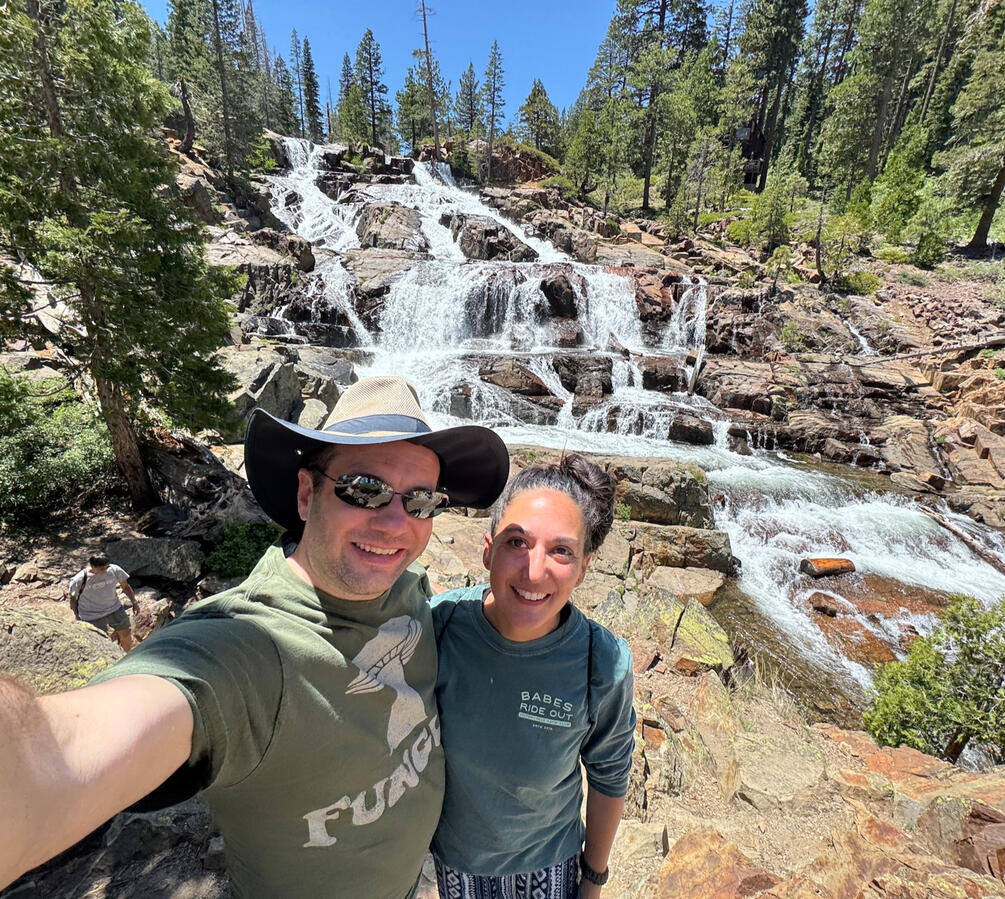 Untitled Michael and Michelle selfie in front of a series of small waterfalls in the background, surrounded by trees.